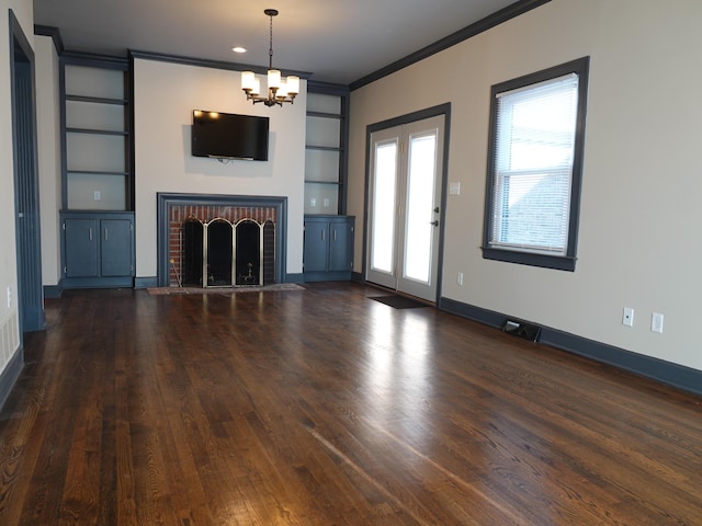 unfurnished living room featuring crown molding, built in features, an inviting chandelier, dark hardwood / wood-style flooring, and a brick fireplace