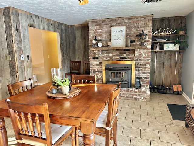 tiled dining area with a fireplace, wooden walls, and a textured ceiling