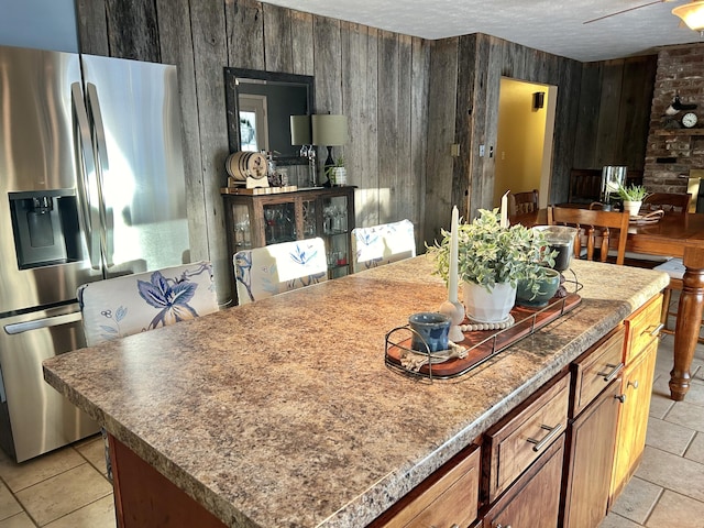 kitchen featuring stainless steel fridge, wooden walls, a textured ceiling, and a kitchen island