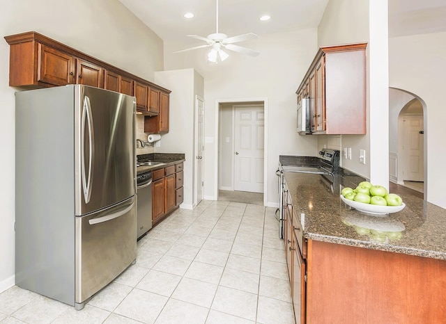 kitchen with dark stone countertops, high vaulted ceiling, light tile patterned floors, and stainless steel appliances