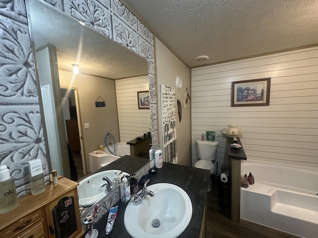 bathroom with toilet, vanity, wooden walls, a textured ceiling, and a washtub