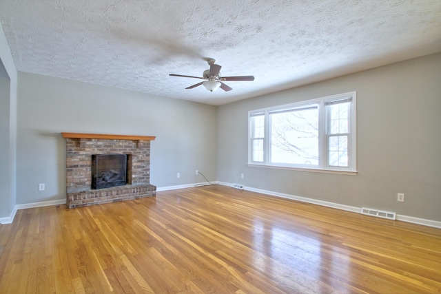 unfurnished living room featuring ceiling fan, a textured ceiling, light hardwood / wood-style flooring, and a fireplace