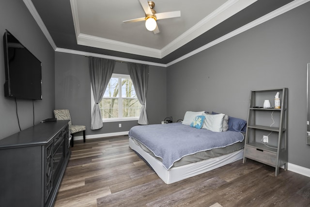 bedroom with ornamental molding, dark wood-type flooring, ceiling fan, and a tray ceiling