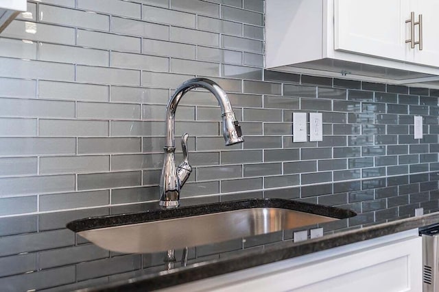 details with sink, dark stone countertops, white cabinets, and decorative backsplash