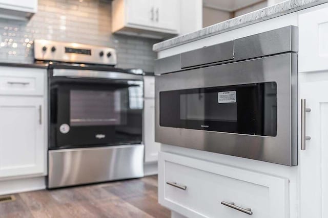 kitchen with oven, white cabinets, backsplash, hardwood / wood-style flooring, and stainless steel range with electric stovetop