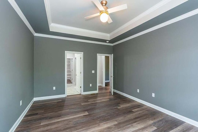 unfurnished bedroom featuring crown molding, a tray ceiling, dark hardwood / wood-style flooring, and connected bathroom