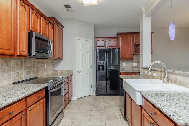 kitchen with light tile patterned floors, hanging light fixtures, backsplash, stainless steel appliances, and light stone countertops