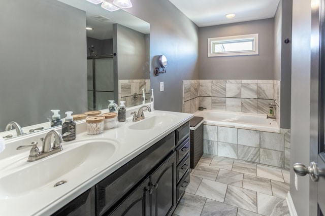 bathroom featuring a relaxing tiled tub, vanity, and tile patterned flooring