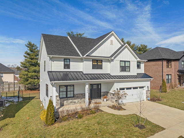 modern farmhouse with a front yard, a standing seam roof, fence, stone siding, and driveway