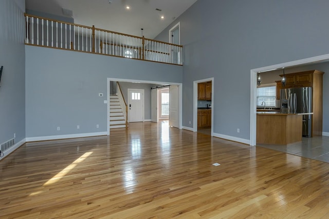 unfurnished living room featuring light wood-type flooring, a towering ceiling, and sink