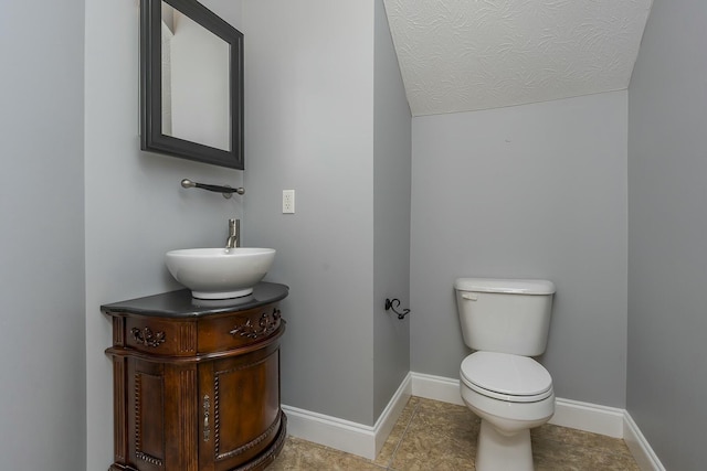 bathroom featuring toilet, vanity, tile patterned flooring, lofted ceiling, and a textured ceiling