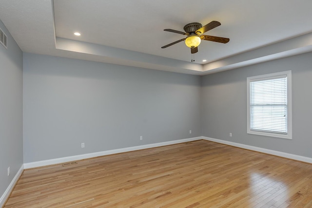 spare room with light wood-type flooring, ceiling fan, and a raised ceiling