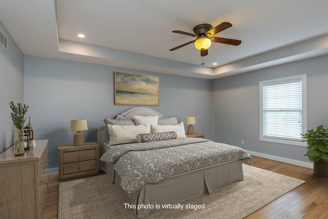 bedroom with ceiling fan, a tray ceiling, and light hardwood / wood-style flooring