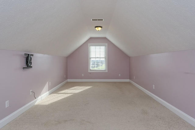 additional living space featuring light carpet, vaulted ceiling, and a textured ceiling