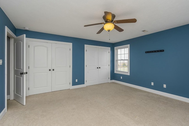 unfurnished bedroom featuring ceiling fan, light carpet, and multiple closets