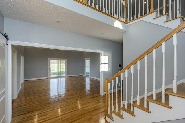 stairs with a barn door, a high ceiling, a textured ceiling, and hardwood / wood-style flooring