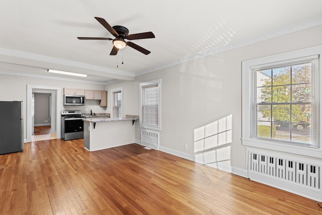 kitchen with radiator heating unit, light brown cabinetry, a breakfast bar area, stainless steel appliances, and light hardwood / wood-style flooring