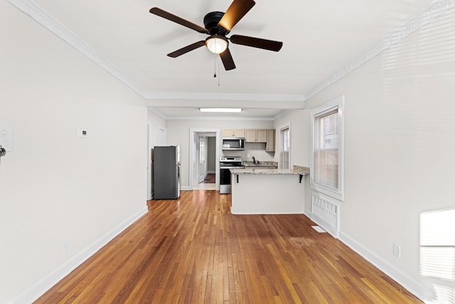 kitchen with light stone countertops, hardwood / wood-style flooring, ornamental molding, and appliances with stainless steel finishes