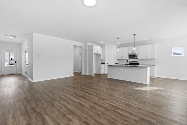 unfurnished living room with a healthy amount of sunlight, baseboards, visible vents, and dark wood-type flooring