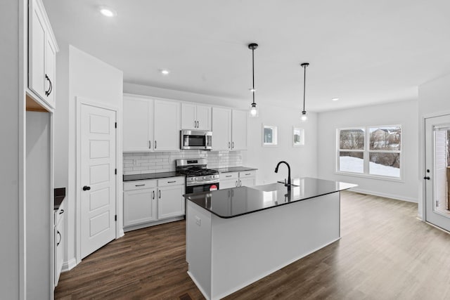 kitchen with white cabinetry, stainless steel appliances, decorative light fixtures, and a center island with sink