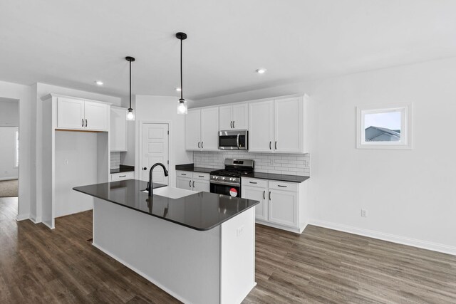 kitchen featuring pendant lighting, appliances with stainless steel finishes, white cabinetry, backsplash, and an island with sink