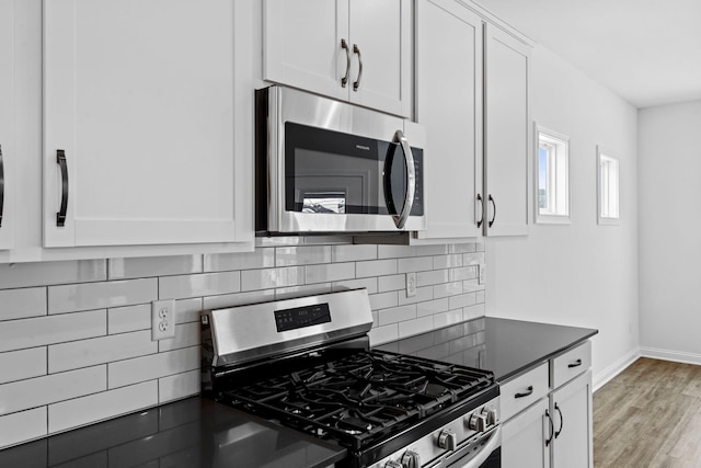 kitchen with tasteful backsplash, dark countertops, wood finished floors, stainless steel appliances, and white cabinetry