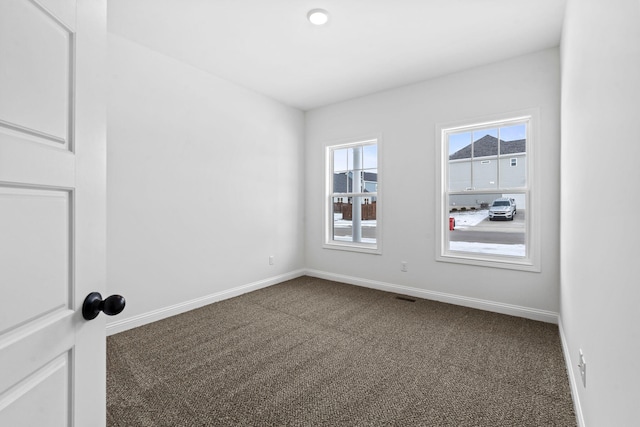 spare room with dark colored carpet, visible vents, and baseboards