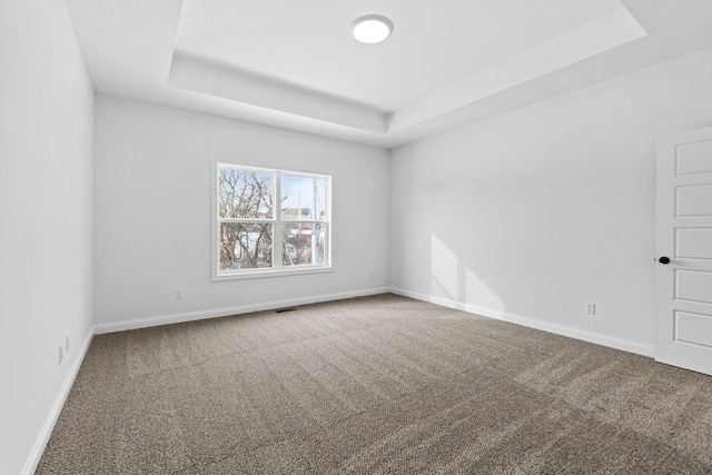 unfurnished room with a tray ceiling, baseboards, and carpet