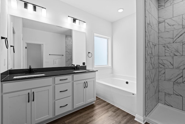 full bath with double vanity, a garden tub, a sink, and wood finished floors