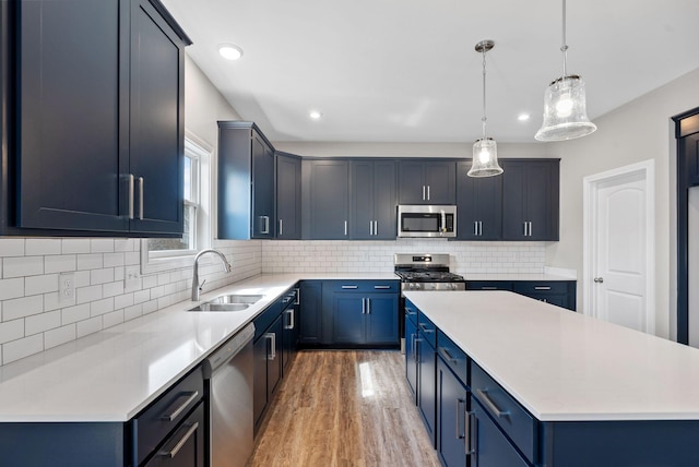 kitchen featuring light wood finished floors, a sink, appliances with stainless steel finishes, blue cabinets, and a center island