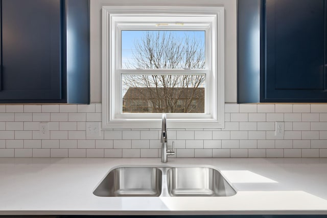 details featuring decorative backsplash, light countertops, blue cabinetry, and a sink