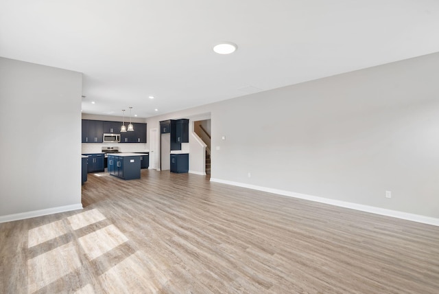 unfurnished living room featuring recessed lighting, baseboards, light wood-style flooring, and stairs