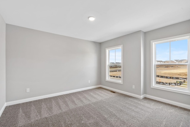 carpeted spare room with a wealth of natural light, visible vents, and baseboards