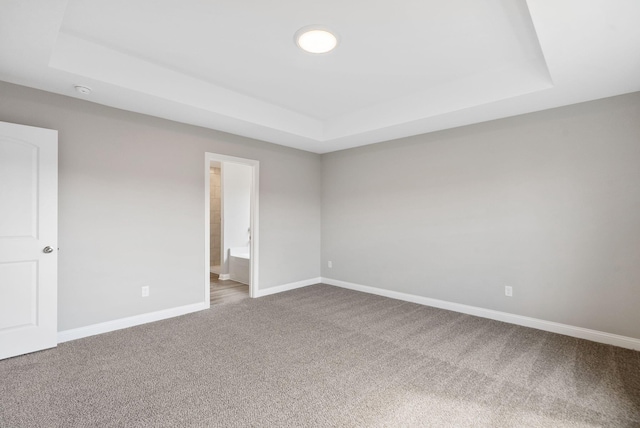 carpeted spare room featuring a tray ceiling and baseboards