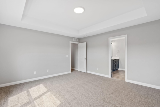 unfurnished bedroom featuring a tray ceiling, baseboards, carpet floors, and connected bathroom