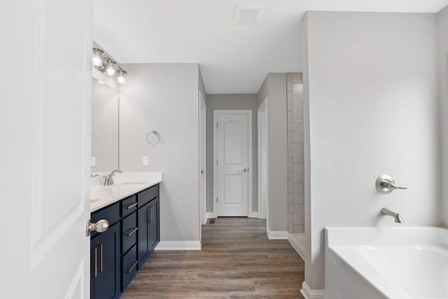 bathroom featuring baseboards, a garden tub, double vanity, wood finished floors, and a sink