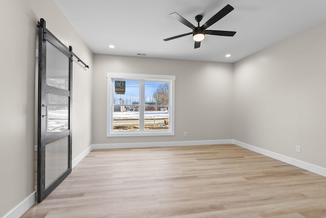 unfurnished room featuring ceiling fan, a barn door, and light hardwood / wood-style flooring