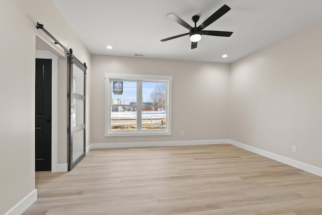 unfurnished room featuring ceiling fan, a barn door, and light hardwood / wood-style flooring