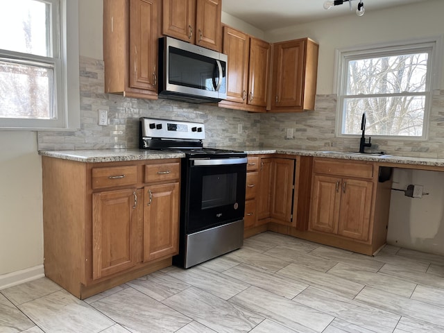 kitchen featuring tasteful backsplash, stainless steel appliances, light stone countertops, and sink