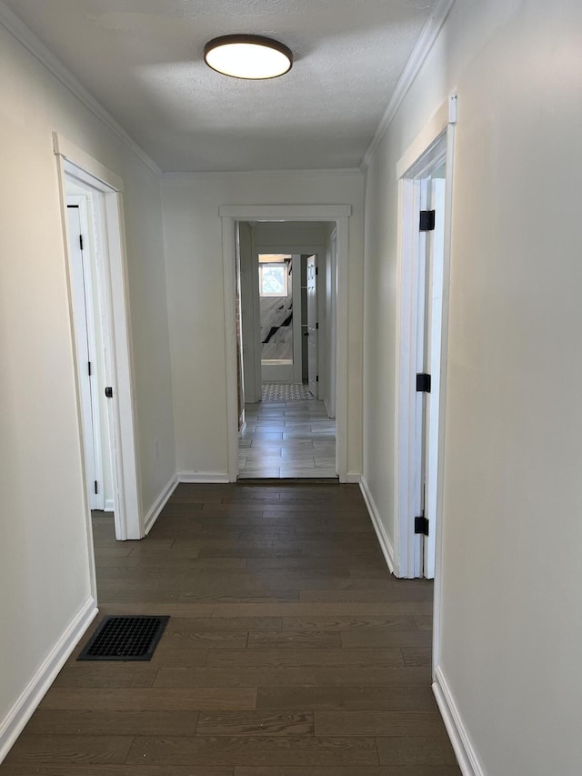 hallway with dark wood-type flooring, ornamental molding, and a textured ceiling