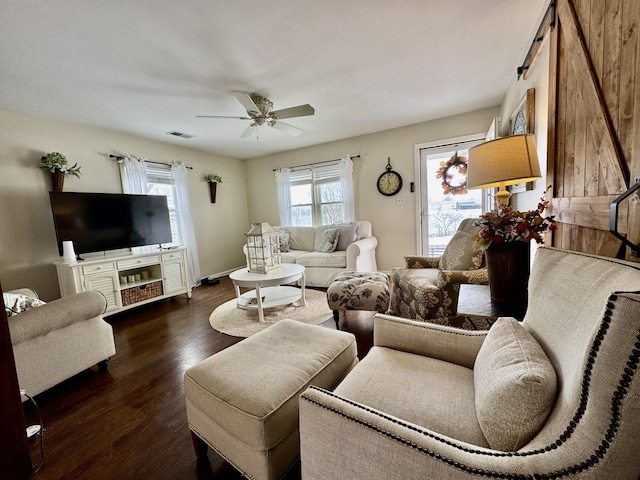 living room with a barn door, dark wood-type flooring, and ceiling fan