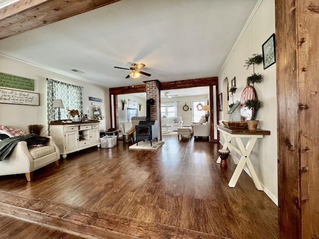 living room featuring ceiling fan, ornamental molding, dark hardwood / wood-style floors, and a wood stove