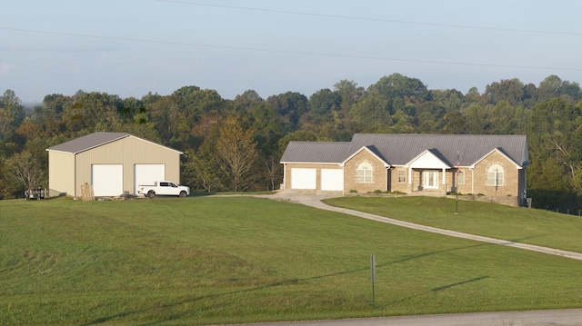 single story home with a detached garage, a view of trees, and a front lawn