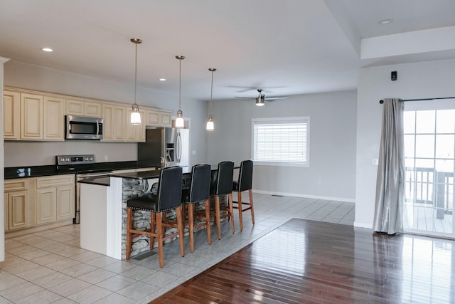 kitchen with appliances with stainless steel finishes, hanging light fixtures, a kitchen breakfast bar, cream cabinetry, and light tile patterned flooring