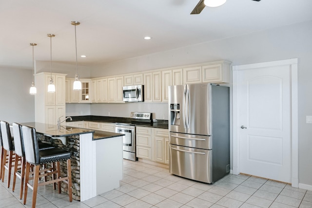 kitchen with stainless steel appliances, hanging light fixtures, a breakfast bar, a center island with sink, and cream cabinetry