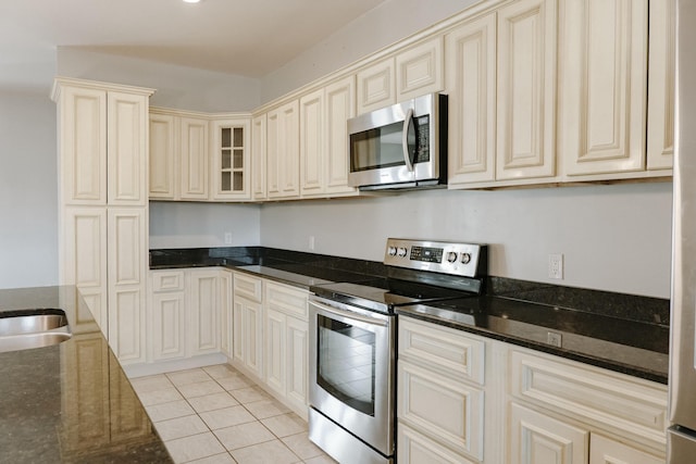 kitchen with light tile patterned flooring, stainless steel appliances, dark stone countertops, and cream cabinets