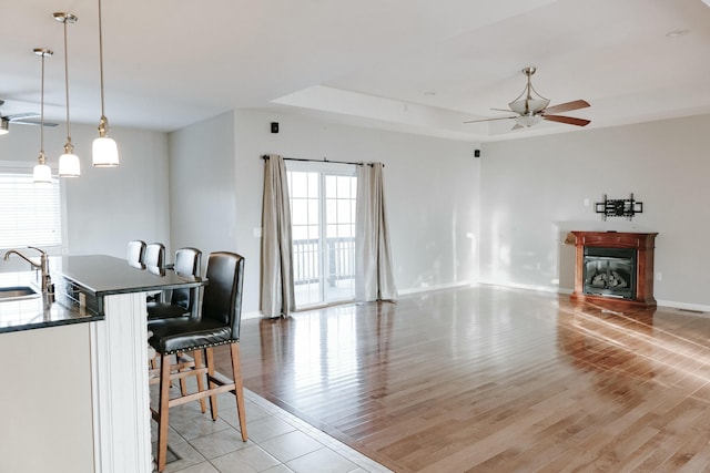 living room featuring sink, light wood-type flooring, a tray ceiling, and ceiling fan