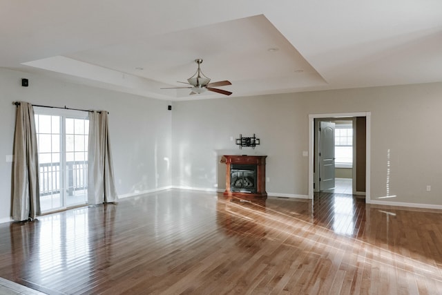 unfurnished living room with hardwood / wood-style flooring, a raised ceiling, and ceiling fan