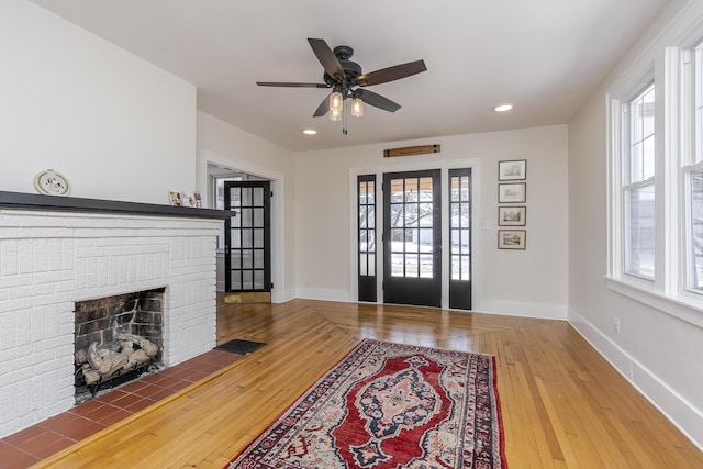 living room with a brick fireplace, hardwood / wood-style flooring, a wealth of natural light, and ceiling fan