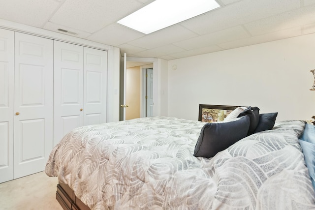 bedroom with a closet, a paneled ceiling, and light carpet